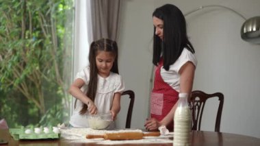 Anne ve kızı yemek pişiriyor. Anne kızına hamuru doğru yoğurmayı öğretiyor. Kız dikkatli bir şekilde un ve yumurtaları cam bir kasede karıştırıyor.