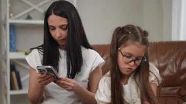 Modern dünyada evde boş vakit geçirmenin zorlukları. Anne internette telefonla konuşuyor, kız annesinden ilgi bekliyor.