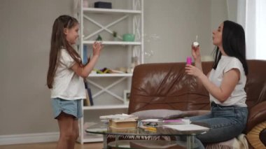 Anne ve kızı modern bir evin oturma odasında eğleniyor ve oynuyorlar. Annesi sabun köpüğü üflüyor ve kızı onları odanın içinde koşarken mutlulukla yakalıyor.