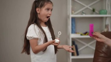 Annesi ve köpüklü sabun köpüğü olan kızı için keyifli bir zaman. Kız neşeyle sabun köpüğü üflüyor.