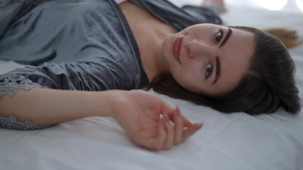 一个穿着睡衣的漂亮姑娘躺在卧室的床上 女孩看着相机笑了 — 图库视频影像