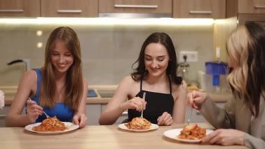 Üç güzel kız mutfak masasında oturuyor ve tabakta çatalla taze pişmiş yemek yiyorlar. Dairenin sahibi davet ettiği arkadaşlarına lezzetli bir yemek ısmarlıyor.