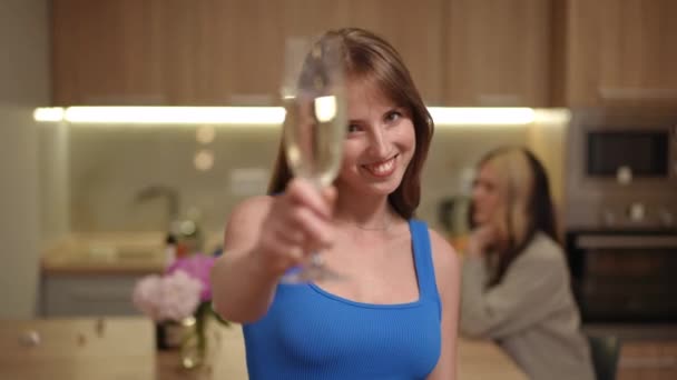 前景では 青いトップの女の子が白いスパークリングワインで長い茎に薄いガラスを手に持っています 女の子は微笑み カメラにグラスを出して その内容を飲みます — ストック動画