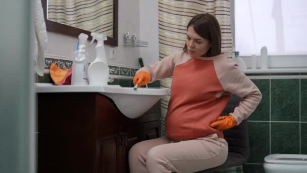 一位戴橡胶手套的孕妇坐在浴室的椅子上 用牙刷清洁水池 — 图库视频影像