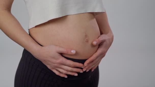 クローズアップ 妊娠中の女性が腹をぶら下げています 認識できない期待する母親は穏やかに立っている白い背景に赤ちゃんと腹部を世話します — ストック動画