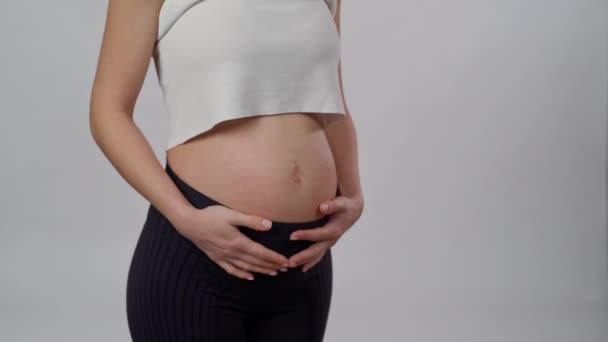 認識できない期待する母親は 白い背景に立って赤ちゃんと腹部を優しく世話します 妊娠中の女性が彼女の腹をストロッキング — ストック動画