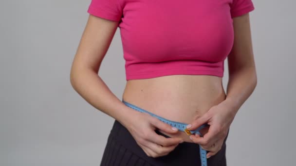 白い背景に立っている間測定テープで彼女の腹を測定するピンクのタンクの上の認識できない妊婦 — ストック動画