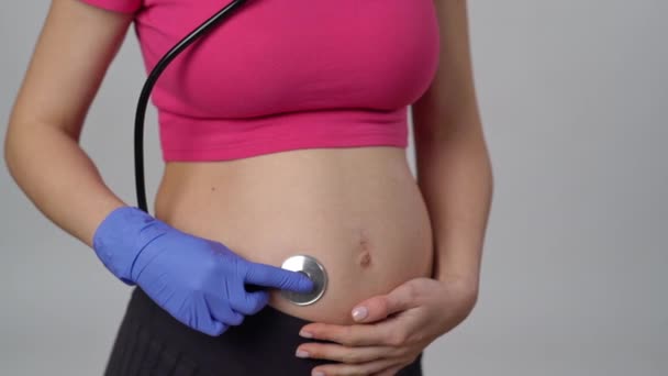 医学的な手袋の中の認識できない妊婦の手は 彼女の腹の上の歯科鏡の頭部を置き 彼女の腹の上にそれを移動し 白い背景に立っています — ストック動画