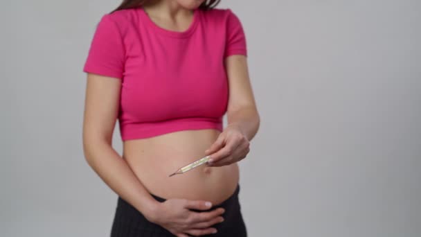 認識できない妊婦は白い背景に立って 彼女の手に水銀の温度計を保持し これはカメラに示しています — ストック動画