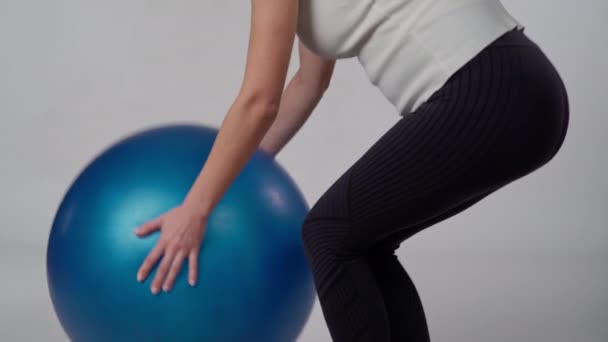認識できない妊婦は青い膨脹可能な体操ボールをもたらします 白いバックグラウンドの女性がボールの上に座り その上にスイング — ストック動画