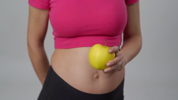 クローズアップ 妊娠中の女性が手に黄色いリンゴを持っています 認識できない女性は白い背景に立っている間 カメラにリンゴを手渡します — ストック動画