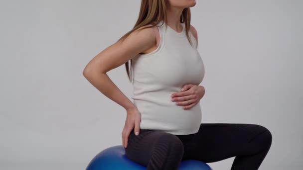 一名无法辨认的孕妇坐在一个白色背景的蓝色适配球上 正在做一项摇晃的健身运动 — 图库视频影像