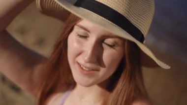 Yakın plan. Hafif kenarlı şapkalı bir kız nehir kıyısında dururken kameraya bakıyor.