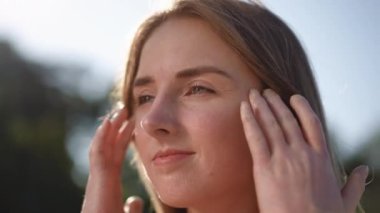 Yakın plan. Ağır çekim. Kız yüzüne beyaz bir koruyucu krem sürerek ellerini ovuyor ve dışarıda dururken gülümsüyor.