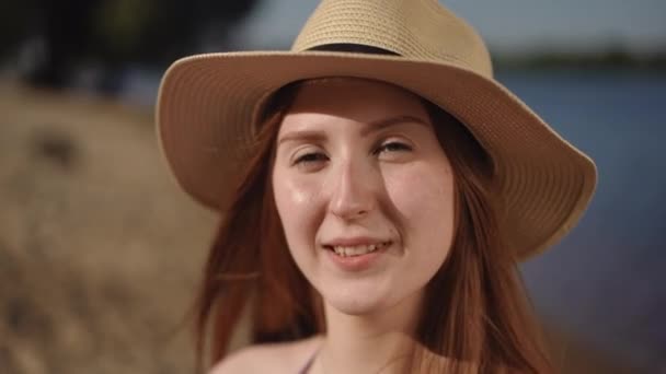 一个头戴帽檐的女孩笑着看着摄像机 站在河岸上 女孩在面颊上涂上白霜 开始揉搓 — 图库视频影像