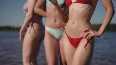 Üç tanınmayan mayo giymiş kız suyun içinde güneşleniyorlar. Bikinili kızların vücut parçaları.