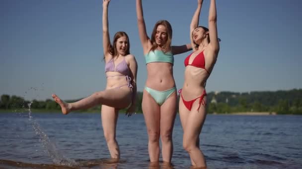 慢动作三个比基尼女孩摆姿势站在水里 姑娘们大声喊着 举手看着摄像机 面带微笑 — 图库视频影像