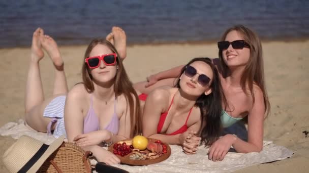 Три Подружки Купальниках Сонцезахисних Окулярах Позують Лежачи Прикритті Піщаному Пляжі — стокове відео