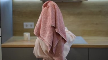 Dikiz aynası. Kafasında pembe havluyla bornozlu bir çocuk mutfakta yemek pişirir, elektrikli ocağın yanında durur.