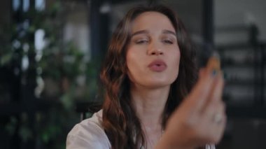 Yakın plan. Dişi bir astrolog bir ritüel gerçekleştiriyor, kameranın önünde elini dumanlı bir mumla teatral bir şekilde hareket ettiriyor. Bir kadın mumu üflüyor ve dikkatlice dumana bakıyor.