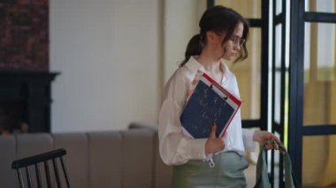 Gözlük takan modern bir iş kadını ofise elinde bir çanta ve elinde belgelerle gelir. Kadın çantasını bırakır ve masaya oturur, dizüstü bilgisayarını açar.