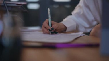 Yakın plan. Beyaz bluzlu tanınmayan bir kadın içeride otururken masasında elinde kalemle duran belgeleri imzalıyor.