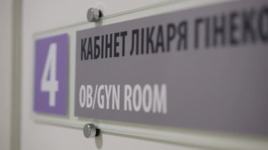 Bu video, duvara asılmış bir tabelanın detaylı yakın çekimini gösteriyor. Kamera, Gyn odasının işaretini göstermek için yakınlaştırıyor..