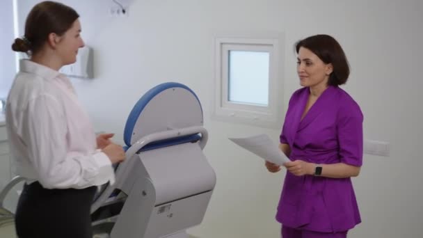 Female Doctor Purple Medical Suit Approaches Patient Holding Paper Documents — Αρχείο Βίντεο