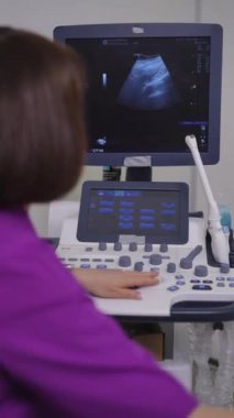 Dikey video. Kadın doktor ultrason taraması yapıyor. Bir kadın ultrason makinesinde çalışıyor ve monitör ekranına bakıyor.