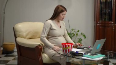 Hamile bir kadın bir kalem alır, hesap makinesine güvenir ve oturma odasındaki cam bir masanın önünde deri koltukta otururken not defterine yazar. Bir kadın konuşuyor ve patlamış mısır yiyor.