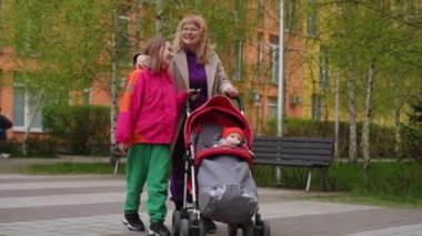 Ağır çekim. Bir anne, bebek arabasını sürerken gülümseyen kızına gülümsüyor. Bebek arabasında küçük bir çocuk oturuyor ve plastik bir şişeden su içiyor. Dışarıda yürüyüş yapan bir aile...