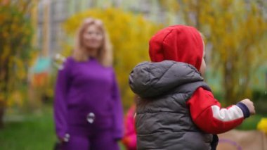 Ağır çekim. Yakın plan. Küçük bir çocuk bahar parkında yürürken elleriyle sabun köpüğü yakalamaya çalışıyor.