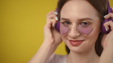 Modaya uygun güneş gözlüğü takan şık ve şık bir kadın parlak ve parlak sarı bir arka plana karşı güvenle poz veriyor.