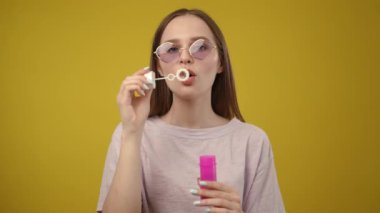 Neşeli ve gülümseyen genç bir kadın parlak ve canlı sarı bir zemin üzerinde renkli bir kapsül tutuyor.