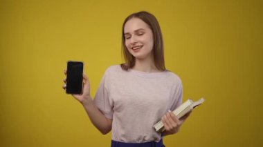 Neşeli ve hayat dolu genç bir kadın neşeli bir şekilde elinde parlak sarı bir zemin üzerine kurulmuş akıllı bir telefon ve bir defter tutuyor.