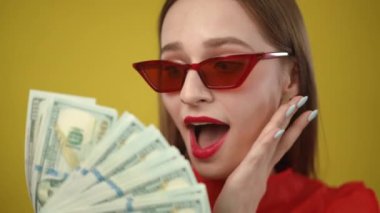 Kırmızı elbiseli şık bir kadın zarif bir şekilde para sergiliyor. Parlak sarı bir fon karşısında.