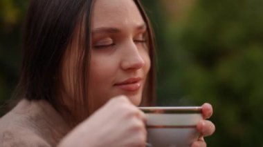 Huzurlu ve huzurlu bir anda, bir kadın güzel doğayla çevrili iken sıcak bir içkinin tadını çıkarıyor.