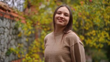 Neşeli genç bir kadın zarif bir şekilde renkli yapraklarla çevrili canlı bir sonbahar bahçesinde duruyor.