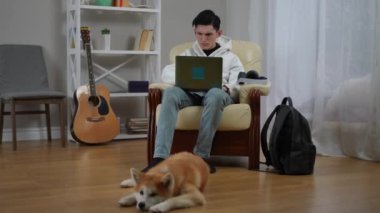 Genç bir insan dizüstü bilgisayarına odaklanır, rahat bir odada, bir köpeğin yerde huzur içinde dinlendiği yerde.