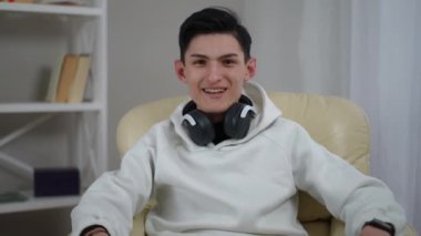 Genç bir birey rahat bir oturma odasında rahat bir şekilde oturur, şık kulaklıklar takar ve ortamın tadını çıkarır.