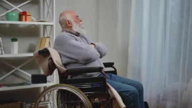 Tekerlekli sandalyedeki yaşlı bir adam, derin düşüncelere dalmış, sessizce etrafı seyrediyor ve düşünüyor.
