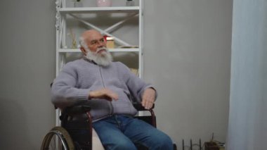 Yaşlı bir adam, sıcak ve davetkar bir yerde, tekerlekli sandalyesinde rahat bir şekilde oturur ve düşünceli bir şekilde düşünür.