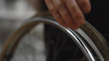 Bir adamın kol parçası ve tekerlekli sandalyesinin tekerleklerinin yakın çekimi.