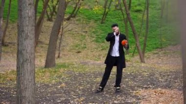 Resmi takım elbiseli bir adam, elinde renkli sonbahar yapraklarıyla çevrili bir ekmekle parkta sessizce durur.