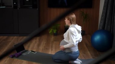 Hamile bir kadın evde yoga yapıyor. Hamilelik boyunca rahatlamaya, forma ve refaha odaklanıyor.
