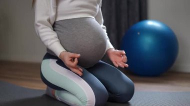 Hamile bir kadın yoga kıyafetleri içinde huzur içinde diz çökmüş doğum öncesi uygunluğu ve derin rahatlamayı incelikle vurguluyor.