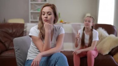 Genç bir kız kanepede oturup annesine bir şey açıklamaya çalışırken hareketler yapar. Anne, ön planda oturuyor çenesi elinde dinleniyor, gözlerini kapatıyor.