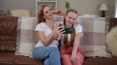 Neşeli bir anne ve kızı, akıllı telefon kullanırken birlikte iyi vakit geçiriyorlar.