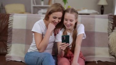Bir anne ve kızın, akıllı telefondaki içeriği izlerken kahkahalarını paylaşması gibi neşeli bir an yaşanıyor.