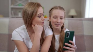 Bir anne ve kızı, akıllı bir telefona bakarken keyifli ve eğlenceli bir anı paylaşıyorlar.